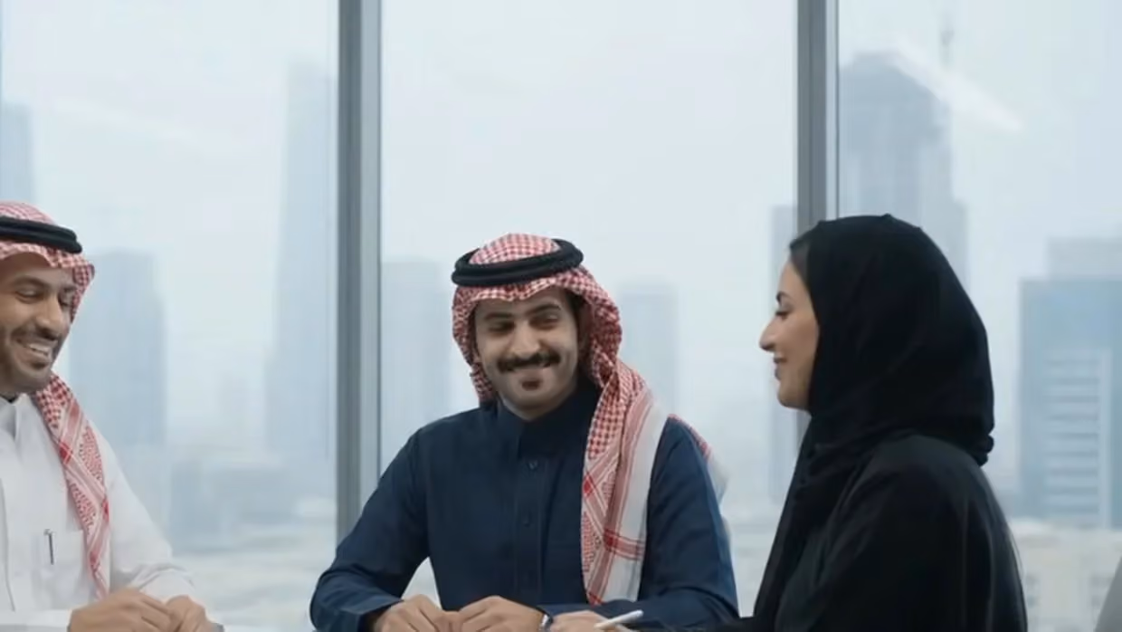 Two colleagues smiling as a third listens across a meeting table